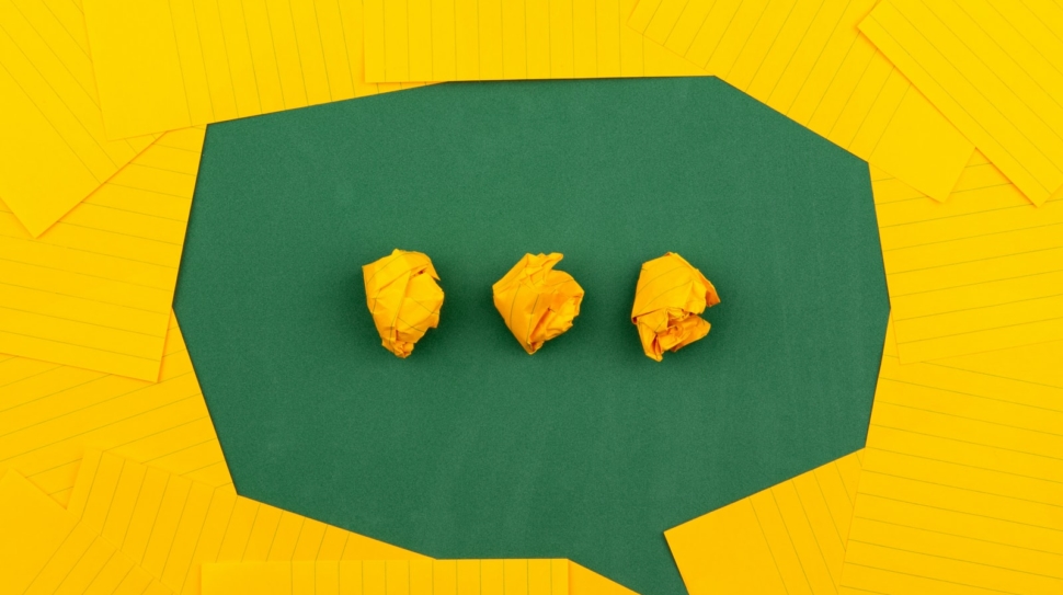 three crumpled yellow papers on green surface surrounded by yellow lined papers